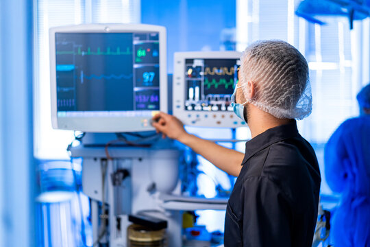 Doc tracks patient vitals. A healthcare worker adjusts monitors displaying patient vitals and medical data in a bright hospital setting.