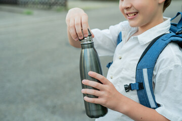 Portrait of a schoolboy with a backpack opens an iron bottle of water. Back to school. Studying.