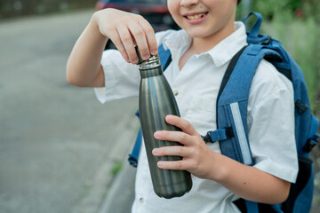 Portrait of a schoolboy with a backpack opens an iron bottle of water. Back to school. Studying.