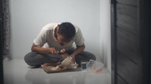 A homeless man is eating food eagerly while sitting on the floor. The footage captures a moment of hunger and survival, reflecting real-life social conditions. Suitable for stock footage about poverty