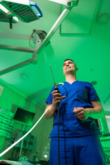 Surgeon ready in green room. A surgeon in blue scrubs stands ready with an instrument in a...