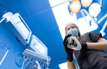 Surgeon preps for operation. A healthcare worker in scrubs holds an anesthesia mask in a bright...