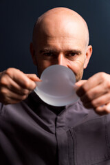 Man shows round object. A man with a bald head is stretching a circular, translucent object in a...