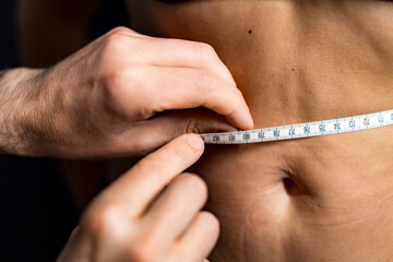 Fitness body measurement. A person measures waist circumference with a tape measure, focusing on body composition and fitness goals.