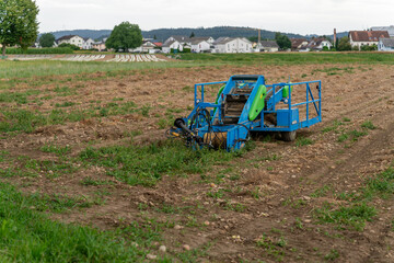 Blue agricultural machine to harvest plants standing on a field. In the background fields and a little rural community.