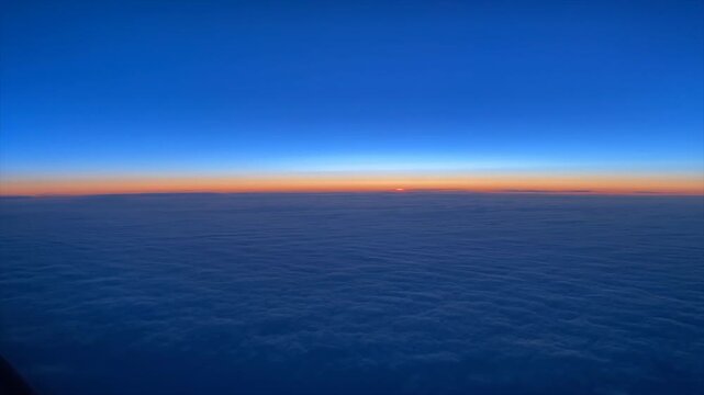 Time-lapse captured from the cockpit of a commercial airliner as the sun rises over the horizon at cruise altitude. The deep blue atmosphere gradually transitions to warm morning light, offering a dra
