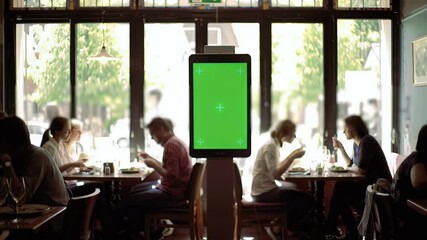 Green Screen Tablet Mockup in Modern Restaurant Setting with Diners. Customizable Digital Display for Menu, Advertising, or Smart Ordering Solution...