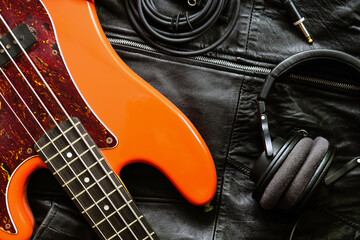 orange electric bass guitar, headphones and cable on a black leather jacket background.