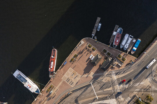 Aerial view of boats docked along the vibrant red-brick quay near Str&Atilde;&para;mbron bridge, contrasting with the dark water and bustling city streets, Stockholm, Stockholm County, Sweden.