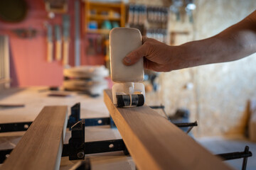 Carpenter hand applying glue to wooden beam surfaces preparing for clamping into large board. Surface sanding, adhesive coating, manual spreading, bonding process, tight compression, extended drying