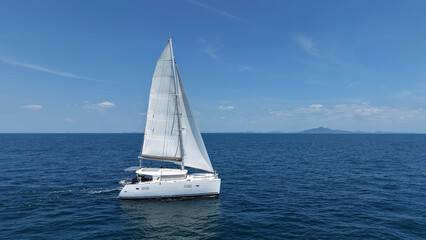 Fototapeta premium Sailing catamaran with open sails. Sailing catamaran in the middle of the sea in a tropical landscape. Sailing boat with open sails. White sailing yacht moving on the sea