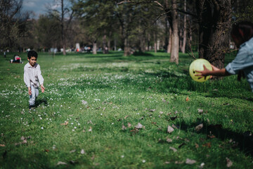 A child dressed in casual clothes playing with a ball outdoors in a lush park with blossoming...