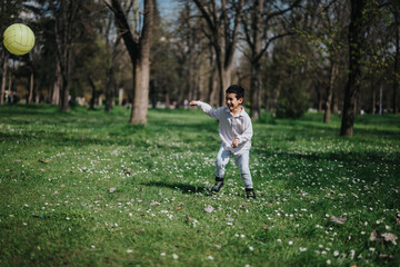 Fototapeta premium A cheerful boy enjoys playing soccer in a grassy park surrounded by trees.
