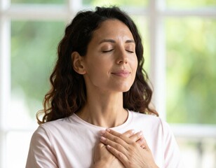A close-up portrait of a woman with closed eyes and hands on her chest, conveying deep gratitude, sincerity, and inner peace.