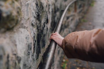 Hand of a woman holding onto a metal railing fixed to a massive stone wall.