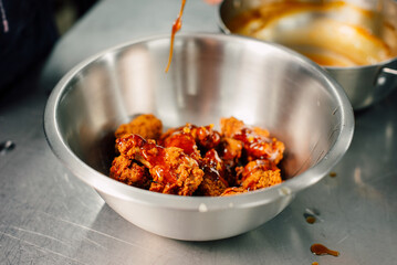 Delicious pieces of fried chicken being generously coated in a rich and flavorful sauce, perfect for any meal