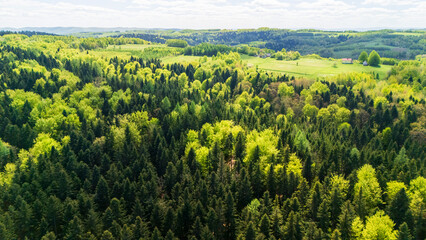 Aerial view of lush green forests blending with open fields under a bright blue sky. This vibrant...