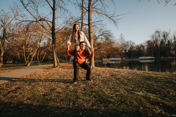 The image depicts a happy couple sharing a joyful piggyback ride in a park at sunset near a serene...