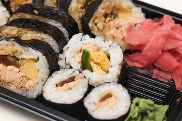 Japanese sushi lunch set. Fresh maki rolls with salmon and vegetables. Pickled ginger and wasabi on side. Black bento tray with delicious rice rolls. Traditional Japanese fast food meal.