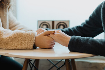 Couple holding hands across a round table, displaying a tender and emotionally supportive moment in...