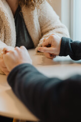 Close-up of couple sitting across from each other, hands held gently over a white table in a quiet,...