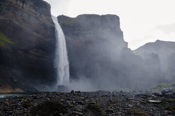 Haifoss waterfall tumbles down steep cliffs amidst a misty atmosphere, showcasing Icelands natural beauty. Lush greenery contrasts with rugged rock formations, creating a stunning vista.