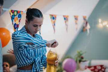 A woman in a striped blouse opening a bottle during a festive birthday party at home, with...