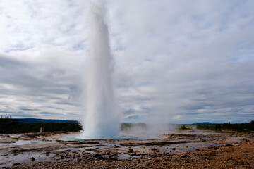 Strokkur Geyser erupts majestically, shooting steam and water high into the air. This natural wonder captivates visitors with its powerful display, surrounded by the serene landscapes of Iceland.