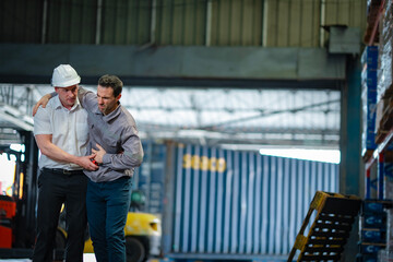 Male employee supports elder colleague after a fall in the warehouse. Useful for content on accident recovery, safety protocols, and labor responsibility.