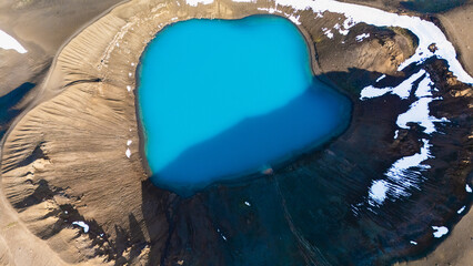 Vivid blue water fills the Krafla crater, surrounded by rugged volcanic terrain and patches of snow. This natural wonder showcases Icelands dramatic geological features and pristine wilderness.