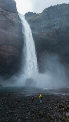 Two hikers explore the enchanting landscape at Haifoss waterfall in Iceland. The powerful flow of...