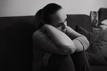 The image captures a woman resting her chin on her arm while sitting on a couch surrounded by a...