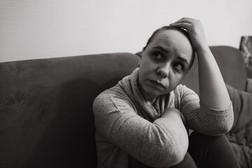 A woman sits on a couch in a dimly lit room her expression thoughtful and contemplative She rests...