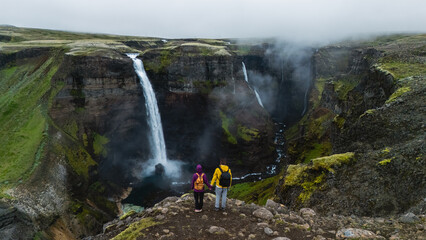 Adventurers stand in awe at the edge of a stunning canyon, overlooking the breathtaking Haifoss...