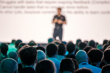 Professionals sit attentively in a large conference room, listening to an engaging presentation on...
