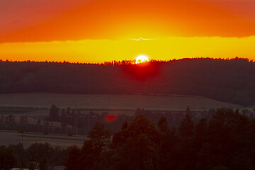 As the sun begins to set over the expansive valley, lush trees stand silhouetted in the foreground, creating a tranquil view