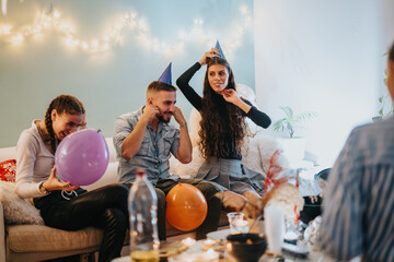 A group of people celebrating a joyful birthday party at home, wearing party hats and interacting...