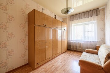 cozy room featuring a large wooden wardrobe, a sofa, floral wallpaper, and a window with curtains