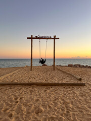 Quarteira, Portugal - November 14, 2023: Swinging at Quartiera beach during sunset, with golden...