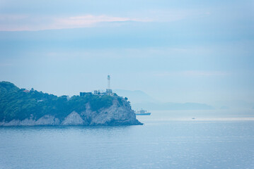 Coastal scene with a hilly landform covered in lush greenery extending into calm, expansive water.
