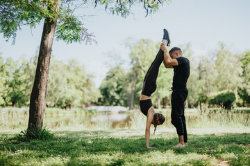 An active couple performs a balance workout together in a grassy park by the lake, showcasing...