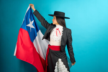 Studio portrait of a latina woman wearing traditional Chilean huasa clothing holding the flag of...