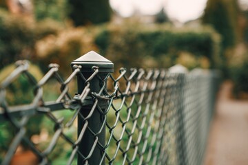 a fence with triangular wire, a close-up on the top of a grey metal post and a green garden background This is a traditional iron mesh fencing for home or commercial use Generative AI