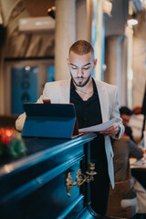 A professionally dressed man reviews documents while using a tablet in an elegant office setting....