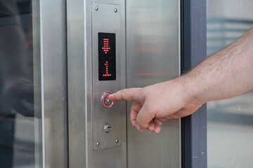 Person pressing the down arrow button on an elevator control panel, displaying the first floor and direction for convenient building access