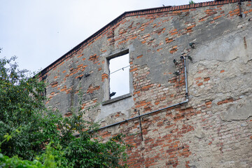 Dilapidated brick wall of an old abandoned building with a broken window, exposed plaster, and...