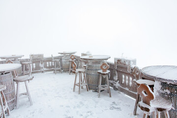 Snow-covered outdoor patio with rustic tables and stools on a foggy winter day
