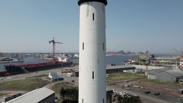 Aerial view of a striking white lighthouse amidst a sprawling industrial harbor filled with ships, cranes, and docks, Dunkirk, Hauts-de-France, France.