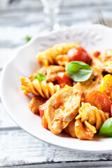 Pasta with chicken breast, cherry tomatoes and fresh basil. Bright wooden background. Close up.	
