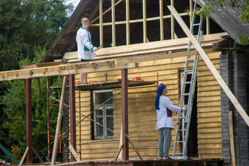 two builders reconstruct a wooden house, repairing a wall and a pediment